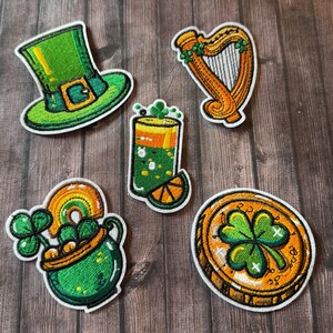 Peut inclure: Ensemble de patchs brodés sur le thème de la Saint-Patrick. Comprend un chapeau de lutin vert, une harpe dorée, un cocktail vert avec une tranche de citron vert, un pot d'or avec un arc-en-ciel et une pièce d'or avec un trèfle.