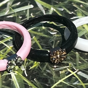 May include: Three silicone rings with a decorative metal flower charm. The rings are pink, black, and white.