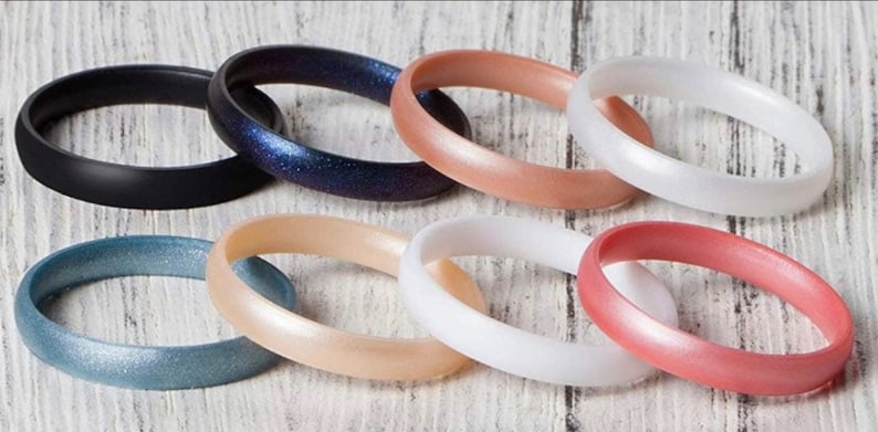 May include: Assortment of eight silicone rings in various colours, including black, blue, beige, white, and pink. The rings have a smooth, glossy finish.
