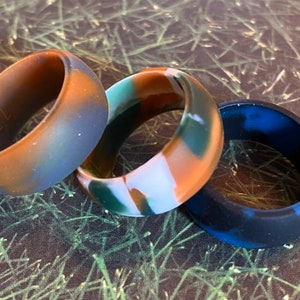 May include: Three silicone rings in different camouflage patterns. The rings are in shades of brown, blue, green, and white.