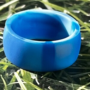 May include: A blue silicone ring with a white stripe down the center. The ring is smooth and has a matte finish.