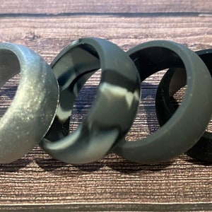 May include: Four silicone rings in different colors and patterns. The rings are black, gray, and a camouflage pattern.