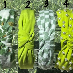 May include: Four green headbands with different patterns. The first headband has a green and white clover pattern. The second headband is a solid green color. The third headband has a green and white checkered pattern. The fourth headband is a solid green color with white pearl accents.