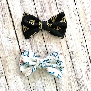 May include: Two bow ties with a black and white pattern of the Deathly Hallows symbol. The top bow tie is black with gold symbols, and the bottom bow tie is white with blue symbols.