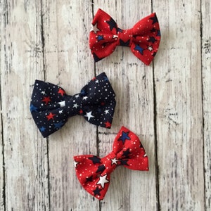 May include: Three red, white, and blue bow ties with a star pattern. The bow ties are made of fabric and are perfect for adding a touch of Americana to any outfit.