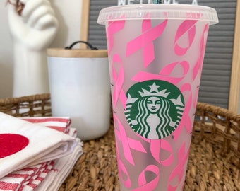 Könnte beinhalten: Ein durchsichtiger wiederverwendbarer Becher mit einem rosa und weißen Design mit rosa Schleifen und dem Starbucks-Logo. Der Becher hat einen Strohhalm.