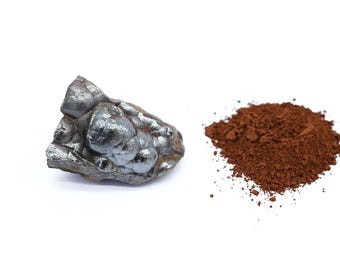 Könnte beinhalten: Ein Stück metallisches, dunkelgraues Hämatit neben einem Haufen rötlich-braunem Eisenoxidpulver. Der Hämatit hat eine raue, strukturierte Oberfläche. Das Pulver ist fein gemahlen und wirkt weich.