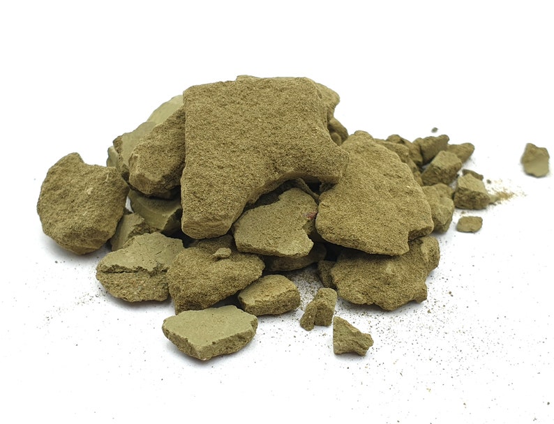 Pode incluir: Um monte de rochas verde-oliva de formato irregular sobre um fundo branco. As rochas t&ecirc;m superf&iacute;cies &aacute;speras e texturizadas e variam em tamanho. Fragmentos menores est&atilde;o espalhados na base da pilha.
