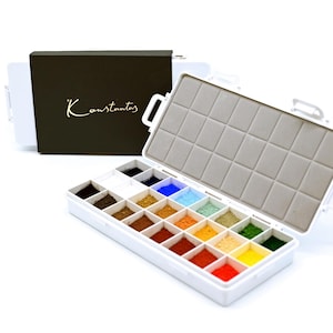 May include: A white watercolor paint set with a variety of vibrant colors. The set includes a dark brown box with the gold text "Konstantus". The paint set is open, revealing a grid of colorful paints.