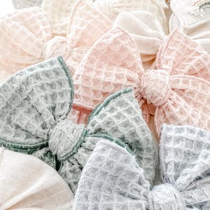 Puede incluir: Una colección de lazos para el pelo hechos a mano de tela en varios colores, incluyendo rosa, verde y gris. Los lazos están hechos con una tela texturizada y tienen un diseño simple y elegante.