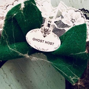May include: Black and green fabric headband with a white lace trim and a white oval tag that says "Ghost Host".