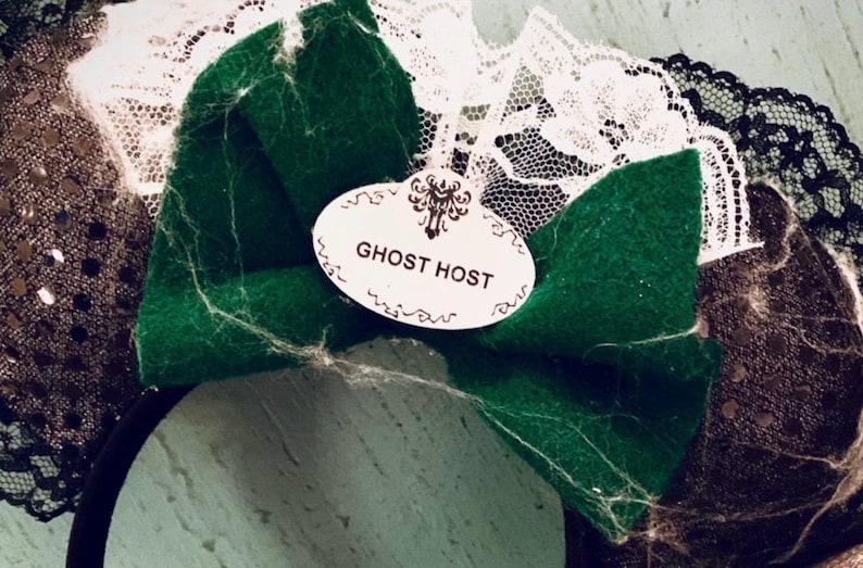 May include: Black and green fabric headband with a white lace trim and a white oval tag that says "Ghost Host".