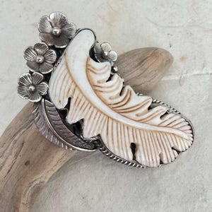 May include: A silver ring with a carved white bone feather design and five silver flower accents.