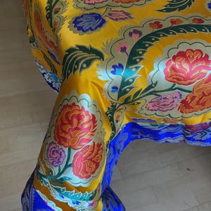 Può includere: Una tovaglia gialla con un bordo blu e un motivo floreale. I fiori sono rossi, rosa, blu e verdi.