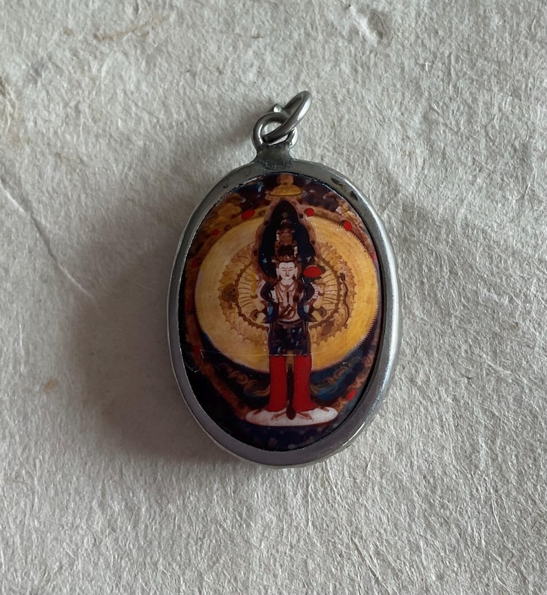 May include: A silver oval pendant with a colorful image of a deity inside. The image is surrounded by a gold halo and a blue and white background.