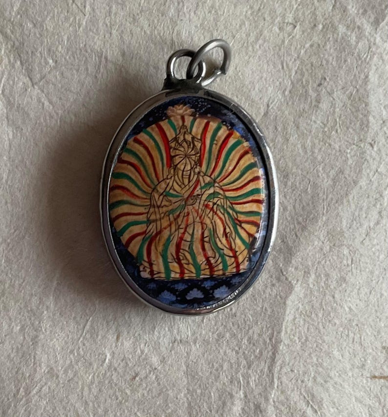 May include: Silver oval pendant with a colorful image of a seated figure with a halo. The figure is surrounded by a radiating pattern of green, red, and yellow stripes.