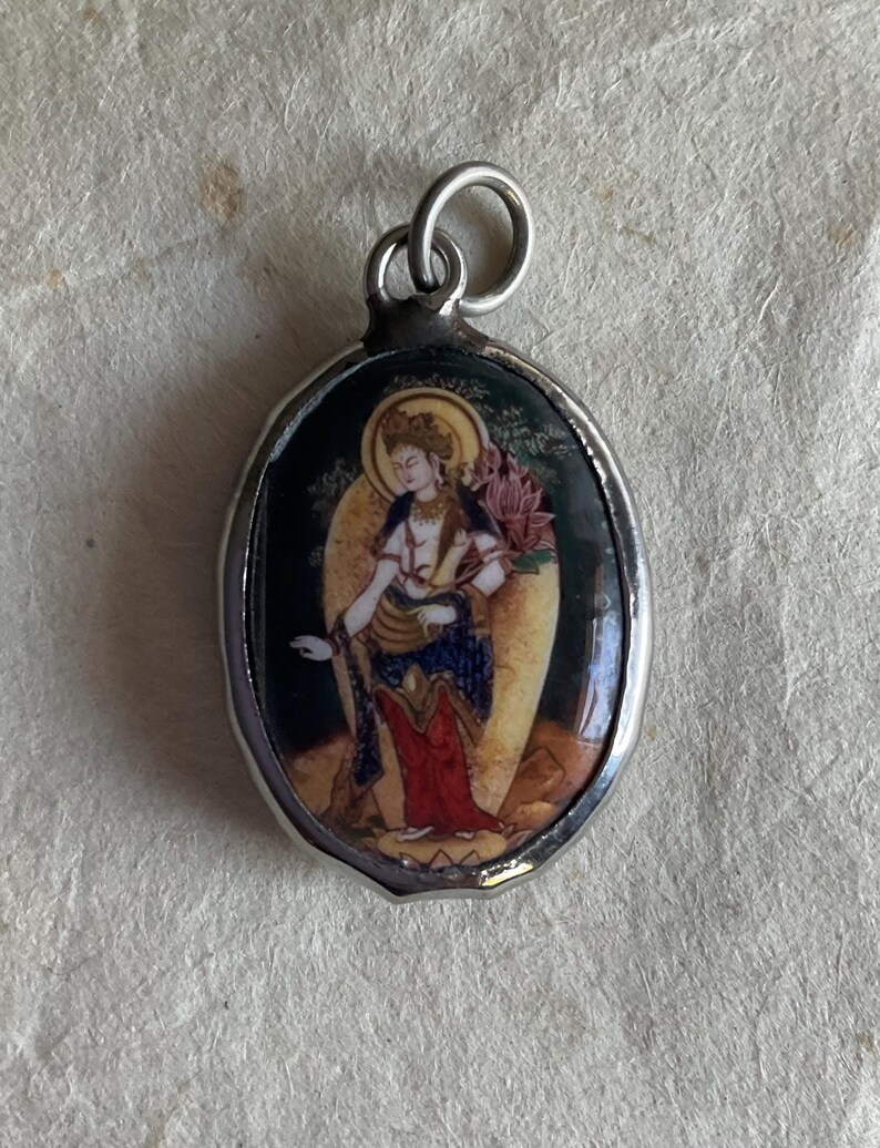 May include: Silver oval pendant with a colorful image of a woman holding a lotus flower.
