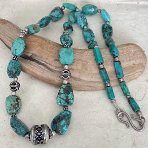 May include: A turquoise necklace with silver detailing. The necklace features irregularly shaped turquoise beads and silver beads. The necklace is secured with a silver hook clasp. The necklace is approximately 45 cm in length.