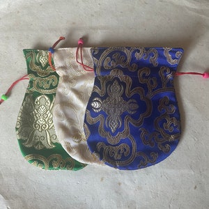 May include: Three small drawstring pouches in green, cream, and blue, each with a gold floral pattern. The pouches have red drawstrings with colorful beads. The pouches are made of a shiny fabric.