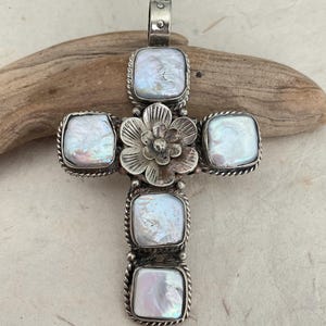 May include: A silver-toned cross pendant featuring five square, iridescent pearl-like stones. The cross has a floral accent at the center and a twisted rope-like border around each stone. The pendant is approximately 3 inches in length.