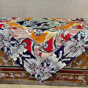 May include: A decorative table with a colorful, patterned cloth. The cloth features a mix of floral and dragon motifs in red, blue, yellow, and white. The table has a red frame with ornate gold and floral detailing.
