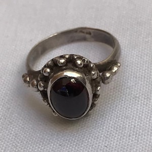 May include: A silver ring with a black oval gemstone set in a beaded bezel. The ring has a simple band and a delicate design.