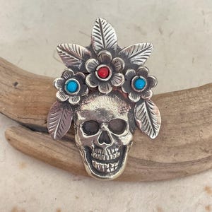 May include: A white ceramic mug with a black handle and the text "But First, Coffee" in a black, handwritten-style font. The mug is on a white surface.