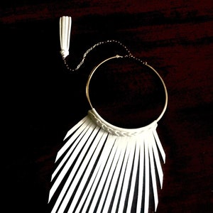 May include: A white leather choker necklace with a fringe of thin leather strips hanging down. The necklace has a gold chain and a small white tassel.