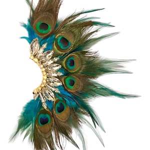 May include: A peacock feather hair comb with a gold base and clear crystal embellishments. The feathers are brown, teal, and green.