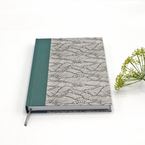 May include: A teal blue hardback journal with a black and white wave pattern on the cover. The journal has a teal blue spine and a ribbon bookmark.