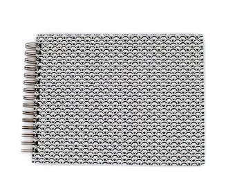 May include: A spiral-bound notebook featuring a repeating black and white fan-shaped pattern across the front cover. The binding consists of a series of dark metal wire loops positioned along the left side of the rectangular notebook.