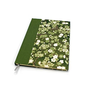 Op de afbeelding: Een notitieboek met harde kaft, een effen donkergroene stoffen rug en een voorzijde versierd met een dicht patroon van witte en lichtgroene kersenbloesems op een donkergroene achtergrond, inclusief een dun grijs leeslint.