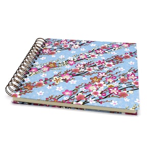 Könnte beinhalten: Ein blaues Spiralblock mit einem Blumenmuster mit rosa und weißen Blüten auf hellblauem Hintergrund.