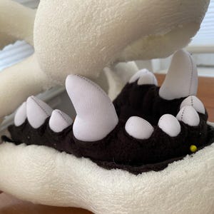 May include: Close-up of a white foam head with a black and white fabric mouth. The mouth is open and has a row of white teeth. The foam head is used for making a costume.