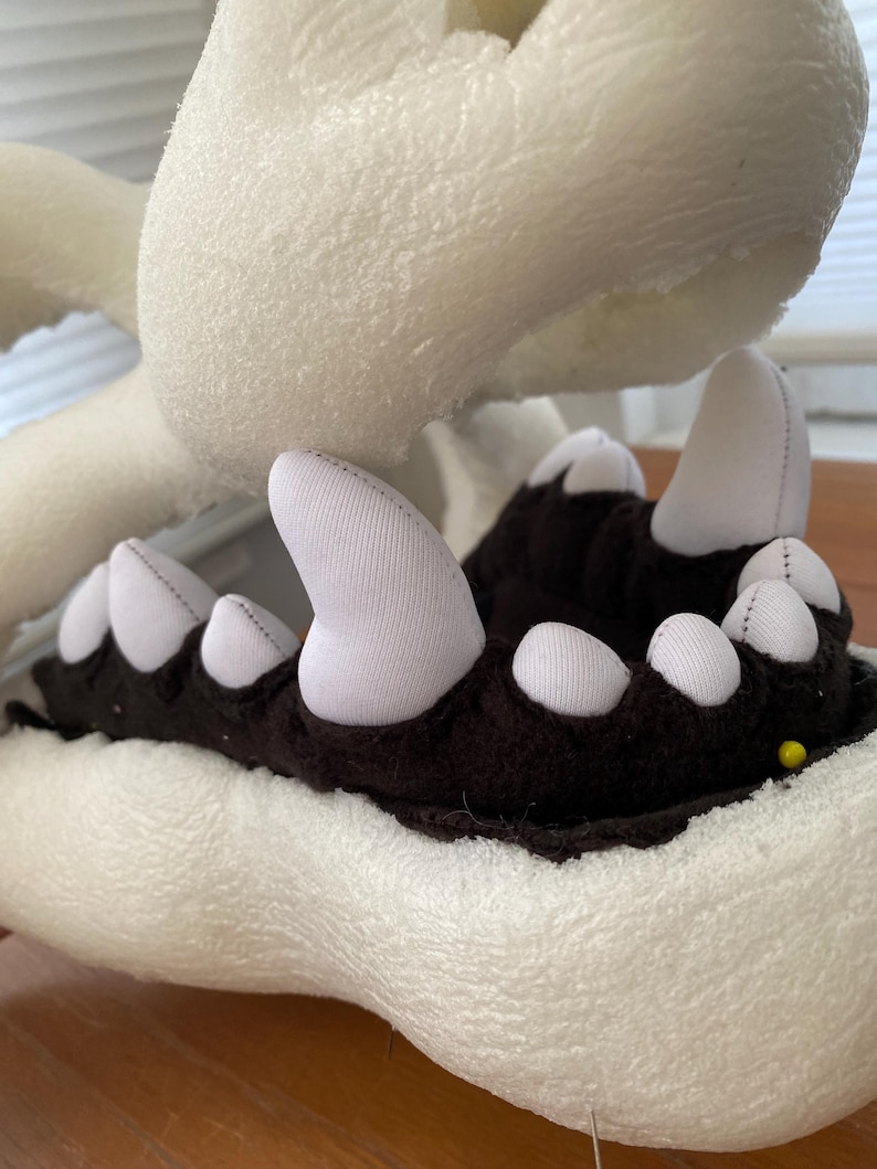 May include: Close-up of a white foam head with a black and white fabric mouth. The mouth is open and has a row of white teeth. The foam head is used for making a costume.
