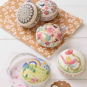 Op de afbeelding: Vier ronde stoffen meetlinten met verschillende ontwerpen. De ontwerpen omvatten een mandala, een bloemenpatroon, een regenboog en een vogel met een hartballon. Elk lint heeft de tekst "Beautifully with Pony" erop gedrukt.
