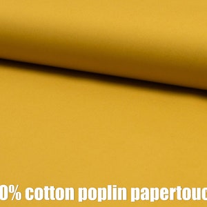 May include: A close-up of a smooth, mustard yellow fabric. The fabric is 100% cotton poplin papertouch.