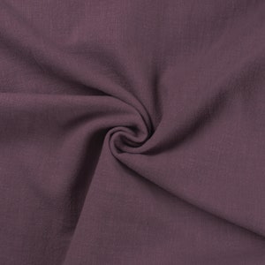 May include: A close-up of a soft, textured fabric in a deep mauve color. The fabric is folded and draped, showcasing its smooth texture.