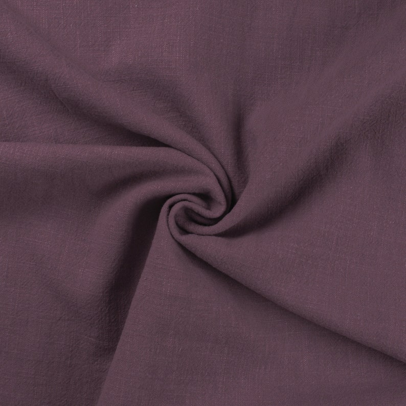 May include: A close-up of a soft, textured fabric in a deep mauve color. The fabric is folded and draped, showcasing its smooth texture.