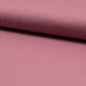 以下が含まれることがあります： 柔らかく滑らかなダスティローズの生地のクローズアップ。生地は控えめな光沢とわずかにテクスチャのある表面をしています。
