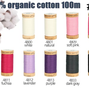 Op de afbeelding: Tien klossen Scanfil 100% biologisch katoengaren, elk 100m lang, in de kleuren wit, naturel, zachtroze, roze, fuchsia, lavendel, paars, donkergrijs en zwart. Elke houten klos is voorzien van de bijbehorende kleurnaam en het nummer.