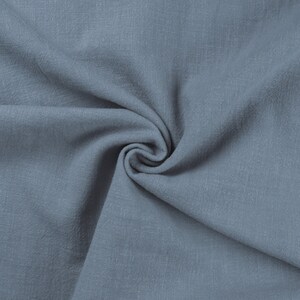 May include: A close-up of a soft, blue fabric with a textured surface. The fabric is folded and draped, creating a smooth, flowing look.