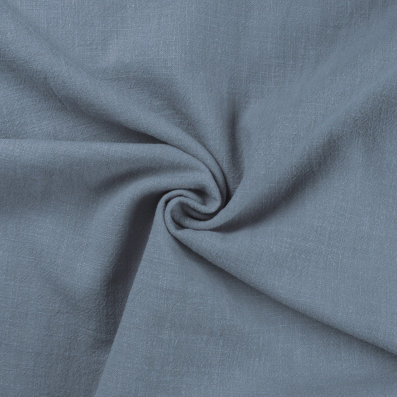 May include: A close-up of a soft, blue fabric with a textured surface. The fabric is folded and draped, creating a smooth, flowing look.