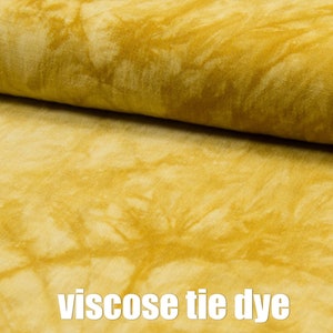 May include: A close-up of a yellow viscose fabric with a tie-dye pattern. The fabric is soft and has a subtle sheen.