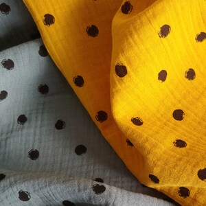 Puede incluir: Dos piezas de tela con lunares negros. Una pieza es de color azul claro y la otra es de color amarillo brillante.