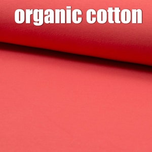 May include: Close-up of a bright red fabric with the text "organic cotton" printed on it.