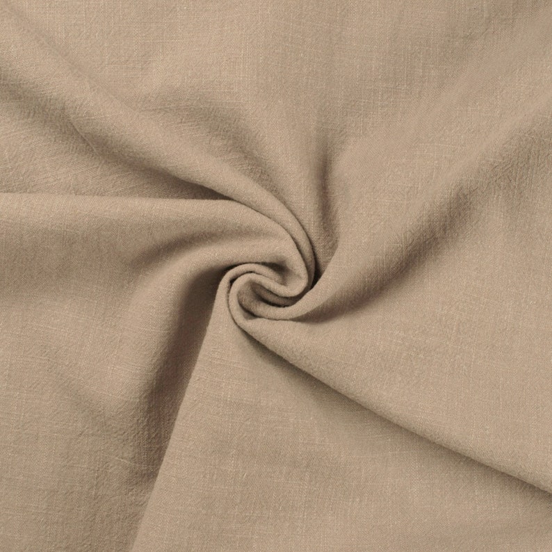 May include: A close-up of a beige fabric with a textured surface. The fabric is folded and draped, creating a soft and inviting look.