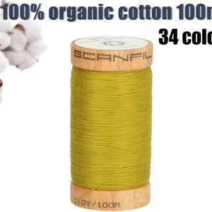 May include: A spool of 100% organic cotton thread in a bright yellow-green colour. The spool is made of wood and has the brand name "Scanfil" printed on it. The thread is 100m long and there are 34 colours available.
