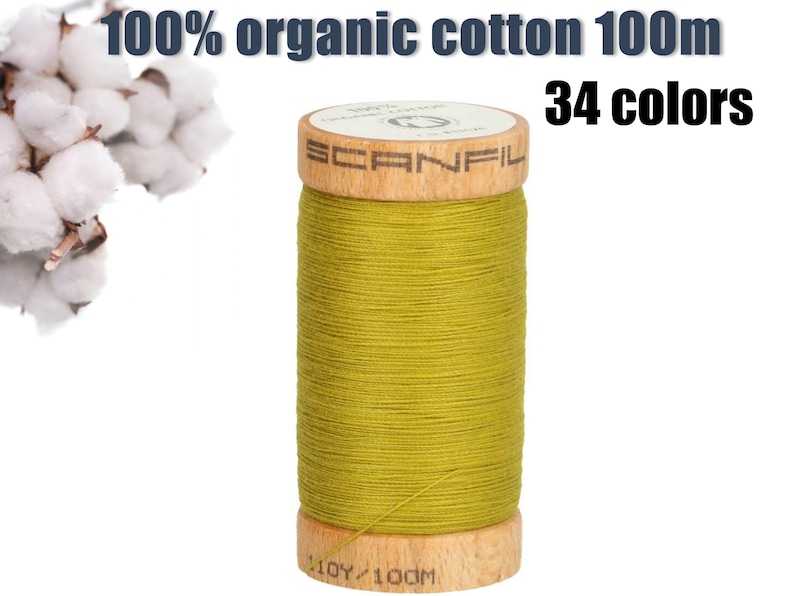 K&ouml;nnte beinhalten: Eine olivgr&uuml;ne Garnrolle mit Holzkern, beschriftet mit Scanfil. Der Text lautet 100% organic cotton 100m und 34 colors. Ein B&uuml;schel wei&szlig;er Baumwollkapseln ist oben links zu sehen, und auf der Basis der Spule steht 110Y/100M.