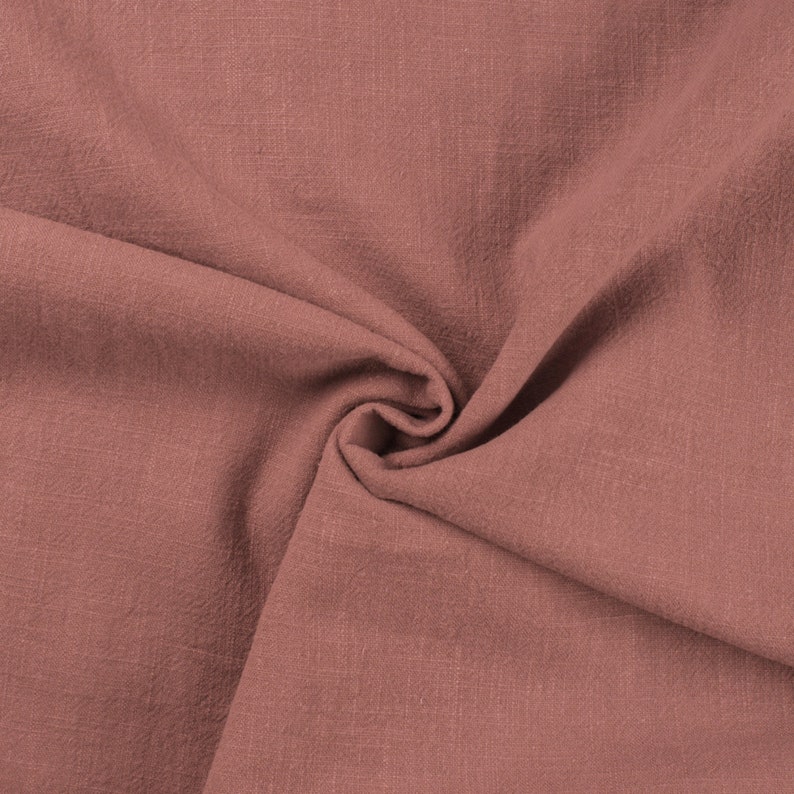 May include: A close-up of a soft, textured fabric in a muted rose color. The fabric is folded and draped, showing its natural wrinkles and folds.